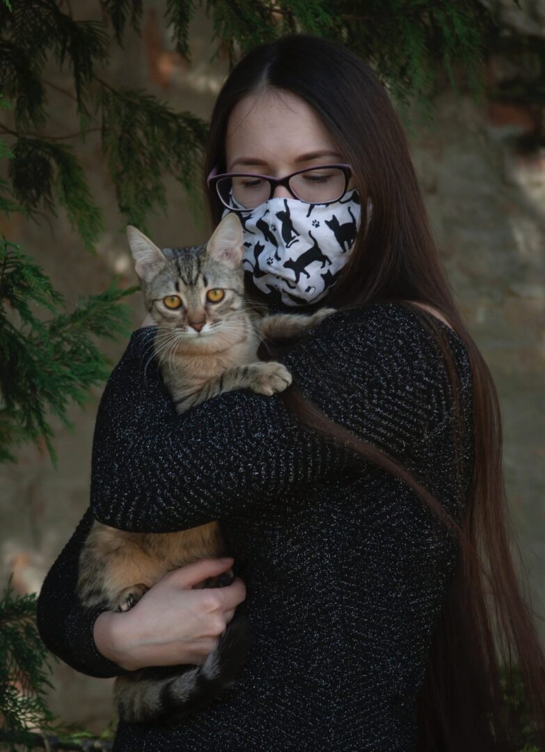 Cat sitter with face mask holding a kitten.